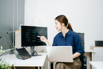 Young female programmer working with tablet and screen displaying code. Modern tech office setup, great for software, coding, IT