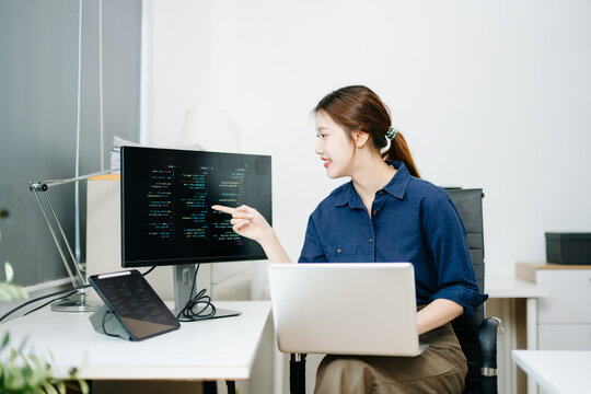 Young female programmer working with tablet and screen displaying code. Modern tech office setup, great for software, coding, IT
