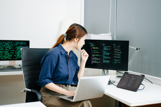 Young female programmer working with tablet and screen displaying code. Modern tech office setup, great for software, coding, IT