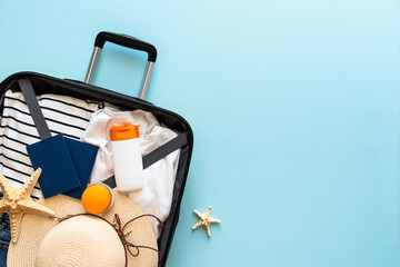 Open Suitcase with summer cloth, shoes and accessories on blue background.