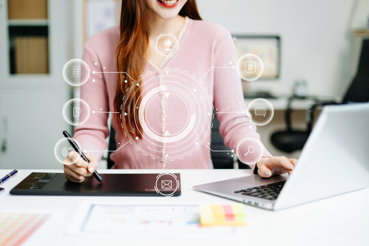 Young graphic designer using pen tablet and laptop at creative desk in modern office. Surrounded by color palettes