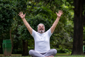 Happy senior indian man laughing spreading hands, relaxing doing yoga at park. Retirement life. Mental health and fitness, Stress free, Fun activity. laugh of therapy senior living 