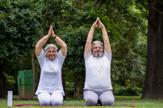 Asian or Indian senior couple doing Yoga and meditation while sitting on yoga mat in the  nature greenery environment. Concept of senior health care after retirement insurance  