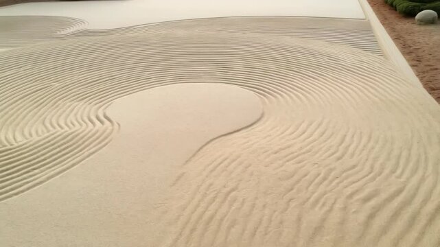 Zen garden sand with raked lines, creating an abstract landscape pattern. Calm, tranquil atmosphere and textures.