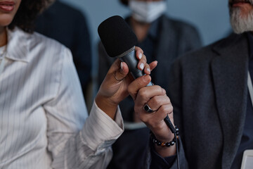 Close up on hand of mature man passing microphone to Black female colleague while sitting in audience space at business conference, copy space