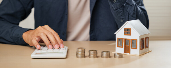 Calculator and house model on a desk with coins stacked. Represents tax savings, property value...