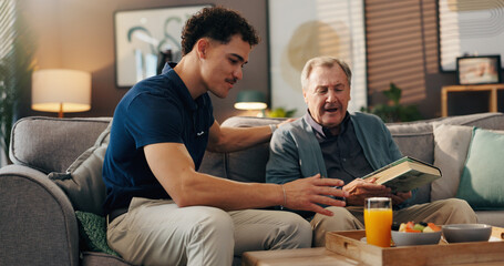 Fototapeta premium Caregiver, elderly man and breakfast on sofa, reading or talk with book, food or nutrition in lounge. Male nurse, senior patient and smile for meal with diet, advice and literature in retirement home