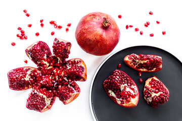 Fresh ripe pomegranate with cut in half and pieces on plate to eat, top view.
