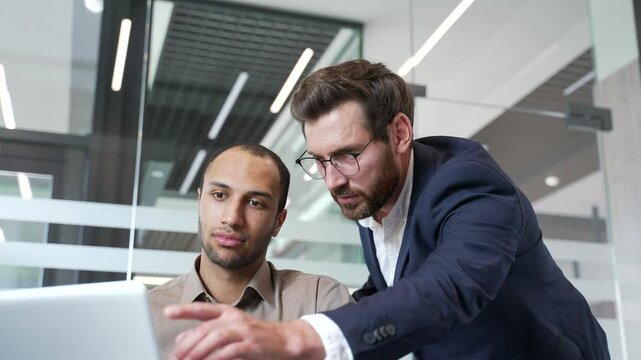 Boss advises subordinate worker. Businessman discussing with colleague at workplace using laptop computer in business office. Male manager explains work issue, consults, talking to employee. Close up