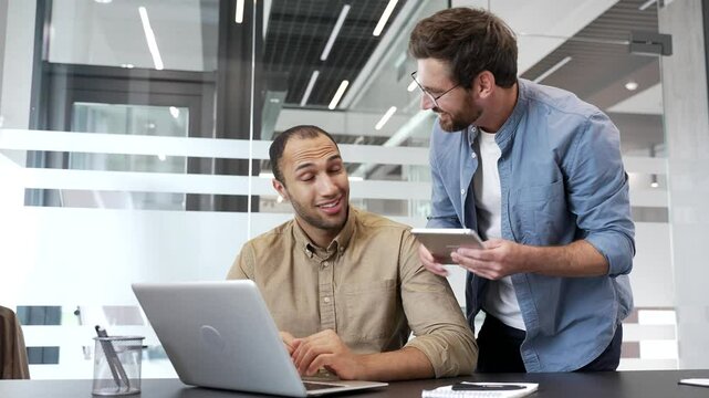 Mature co-worker praises young employee for excellent job at laptop at workplace in business office. Manager motivates colleague worker for job well done. Positive interaction, teamwork, collaboration