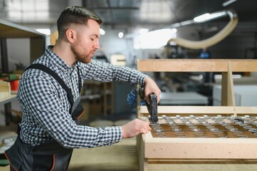 Carpenter using pneumatic stapler building sofa frame in furniture factory
