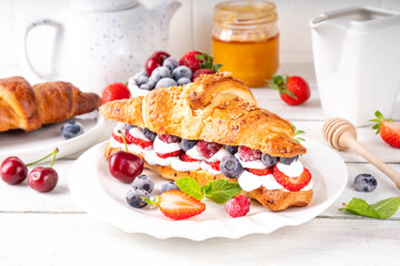 Sweet breakfast croissant sandwich with whipped cream, fresh fruit and berry. Tasty summer lunch or...
