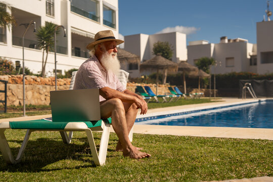 Elderly man enjoying peaceful retirement at a Spanish resort, relaxing barefoot on a sun lounger by the pool on a sunny day, embracing slow living and freedom - Powered by Adobe