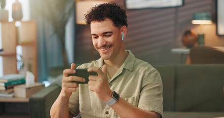 Man, smartphone and earphones for gaming in home, streaming and happy with progress for esports. Gamer, smile and person in house with mobile app for videogame, wireless audio tech and tournament