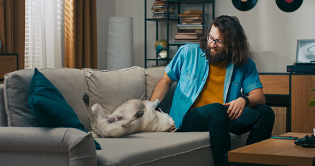 A middle-aged man smiles warmly as he plays with his dog after returning home from work. The loyal pet brings him joy and comfort after a long day.