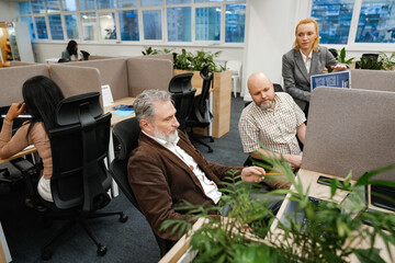 A female employee stands and holds a clipboard while looking at a male employee who is looking at a...
