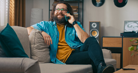 A middle-aged man lounges in the living room, answering the phone to catch up with someone...