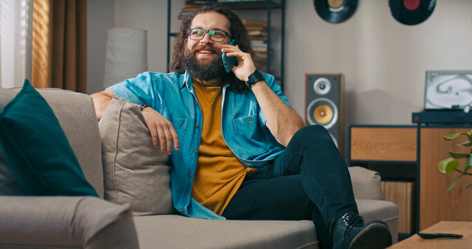 A middle-aged man lounges in the living room, answering the phone to catch up with someone important after a long day. - Powered by Adobe