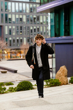 A male intern walks and looks ahead while holding headphones on his head