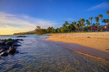 Scenic view of Bel Ombre beach in southern Mauritius with villas, palm trees and sunset light.