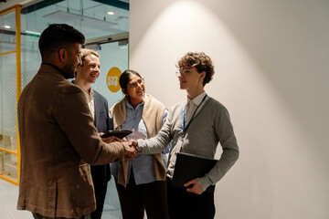 A group of three employees are smiling and talking while one of them shakes the hand of a male...