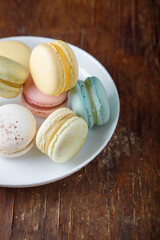 Tender multicolored macaroons with different tastes on white plate, wooden old table background, top view closeup shot