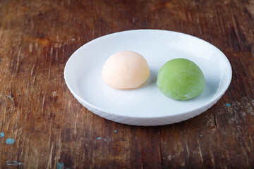 Two pink and green traditional japanese mochi or asian wagashi, rice cakes. Tasty sweets, dessert on wooden brown background, closeup shot