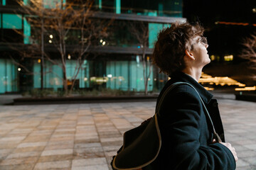 Male intern walking and looking up while holding a backpack on his shoulder, outdoors
