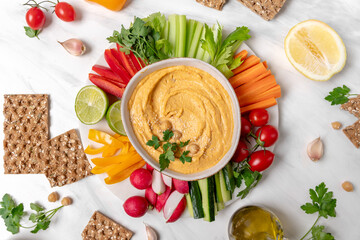 Hummus surrounded by fresh vegetables, crackers, and garnishes, creating a vibrant and healthy snack presentation for gatherings and events	