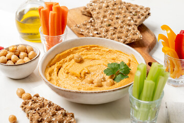 Hummus surrounded by fresh vegetables, crackers, and garnishes, creating a vibrant and healthy snack presentation for gatherings and events	