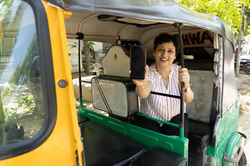 Indian woman showing mobile phone screen while sitting iin auto