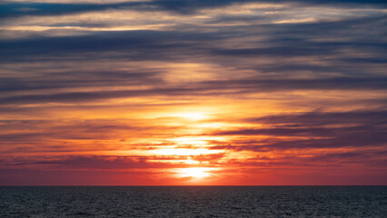 Fiery sunset over the ocean. Intense red and orange hues illuminate the sky and water, creating a...