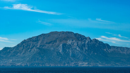 Majestic mountain range rises dramatically from the sea under a clear blue sky. Stunning landscape, natural beauty, serene view