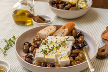 Freshly prepared feta cheese served on a plate with assorted olives, garnished with herbs and lemon slices and crusty bread, traditional Greek or Italian food, Mediterranean diet