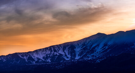 highland mountain landscape of beautiful sunset or sunrise behind nice mountain peaks and slopes in snow and majestic cloudy sky on background