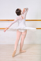 Young adult female ballerina with brown hair practicing in studio. Wearing white tutu and pink...