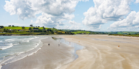 The idyllic beach scene reveals people relaxing and enjoying the weather. The serene atmosphere is enhanced by the rolling hills in the distance.
