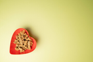 Crunchy, dry, bone shaped pet food or kibble in a red, heart bowl.