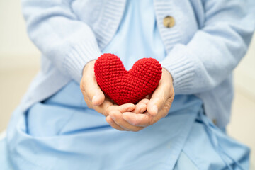 Asian elder senior woman patient holding red heart in hospital.