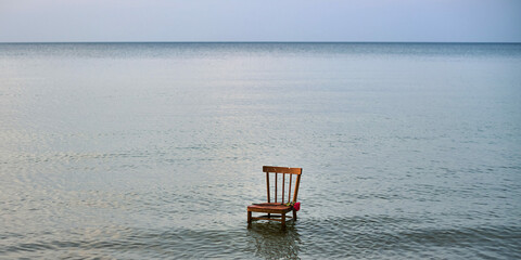Wooden chair stands in calm, vast ocean, symbolizing solitude and contemplation. Stillness of water...