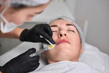 Professional performs lip filler injection on adult woman in clinical setting, highlighting...