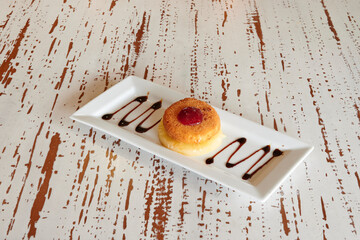 A dessert with a cherry on top is on a white plate. The plate is on a table