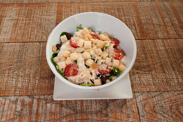 A white bowl of salad with tomatoes and croutons. The bowl is on a wooden table