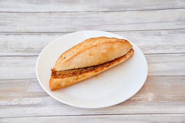 A sandwich is on a white plate. The sandwich is cut in half. The plate is on a wooden table