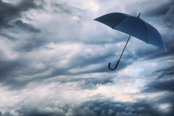 Dark blue umbrella flying in cloudy sky. Stormy weather