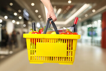 Man holding shopping basket with different food products at supermarket, closeup