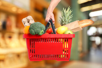 Man holding shopping basket with different food products at supermarket, closeup