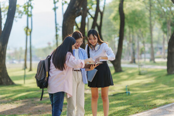 Fototapeta premium Three young women studying together in a park, reviewing notes and preparing for exams while enjoying the beautiful outdoor scenery