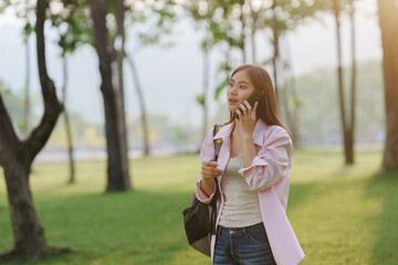 University student walking in park and talking on smartphone, enjoying fresh air and green grass