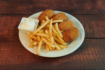 A plate of fried chicken and french fries. The fries are cut into small pieces and are served with a dipping sauce